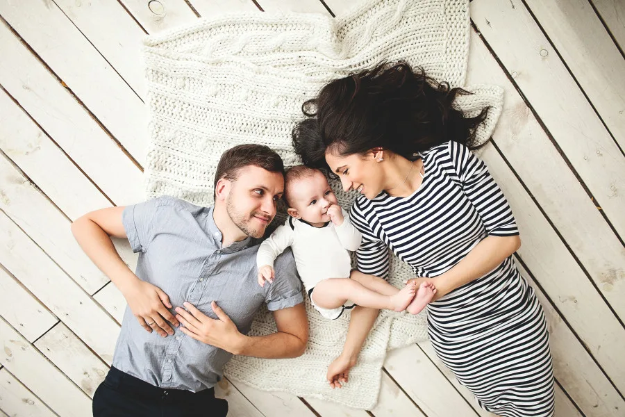 Mother, father, and baby lying happy on a wooden floor.