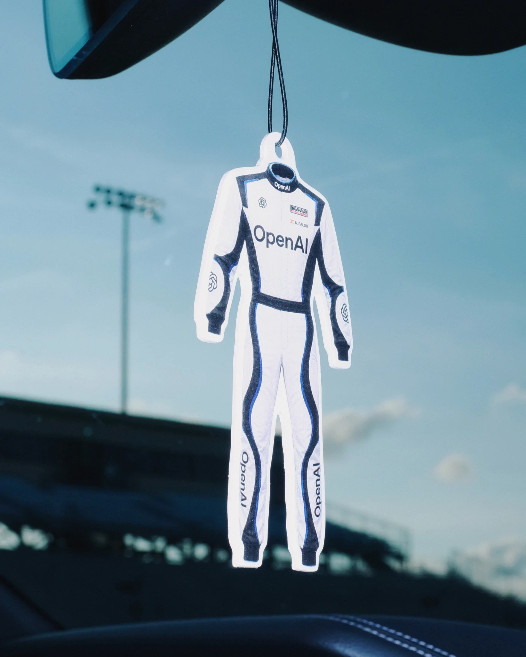 An OpenAI racing suit-shaped accessory hangs beside a racing circuit.