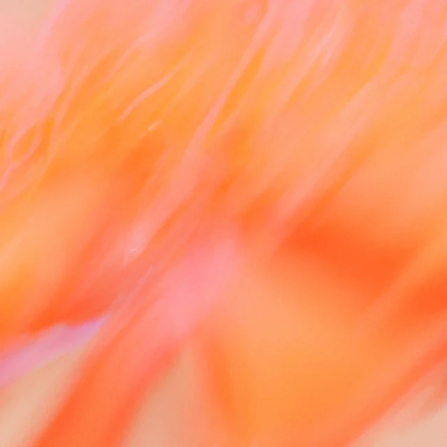 The image shows an abstract blur of orange and pink tones with soft, flowing streaks, creating a warm and dynamic composition. The colors blend together, giving a sense of motion and light.