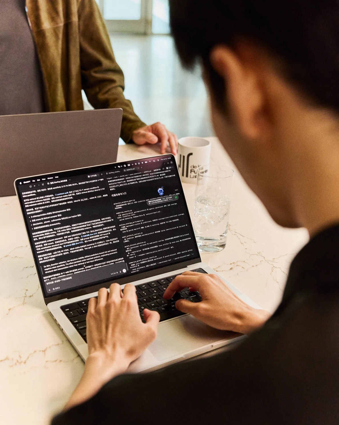 A researcher typing on a laptop with scientific text and code on screen.