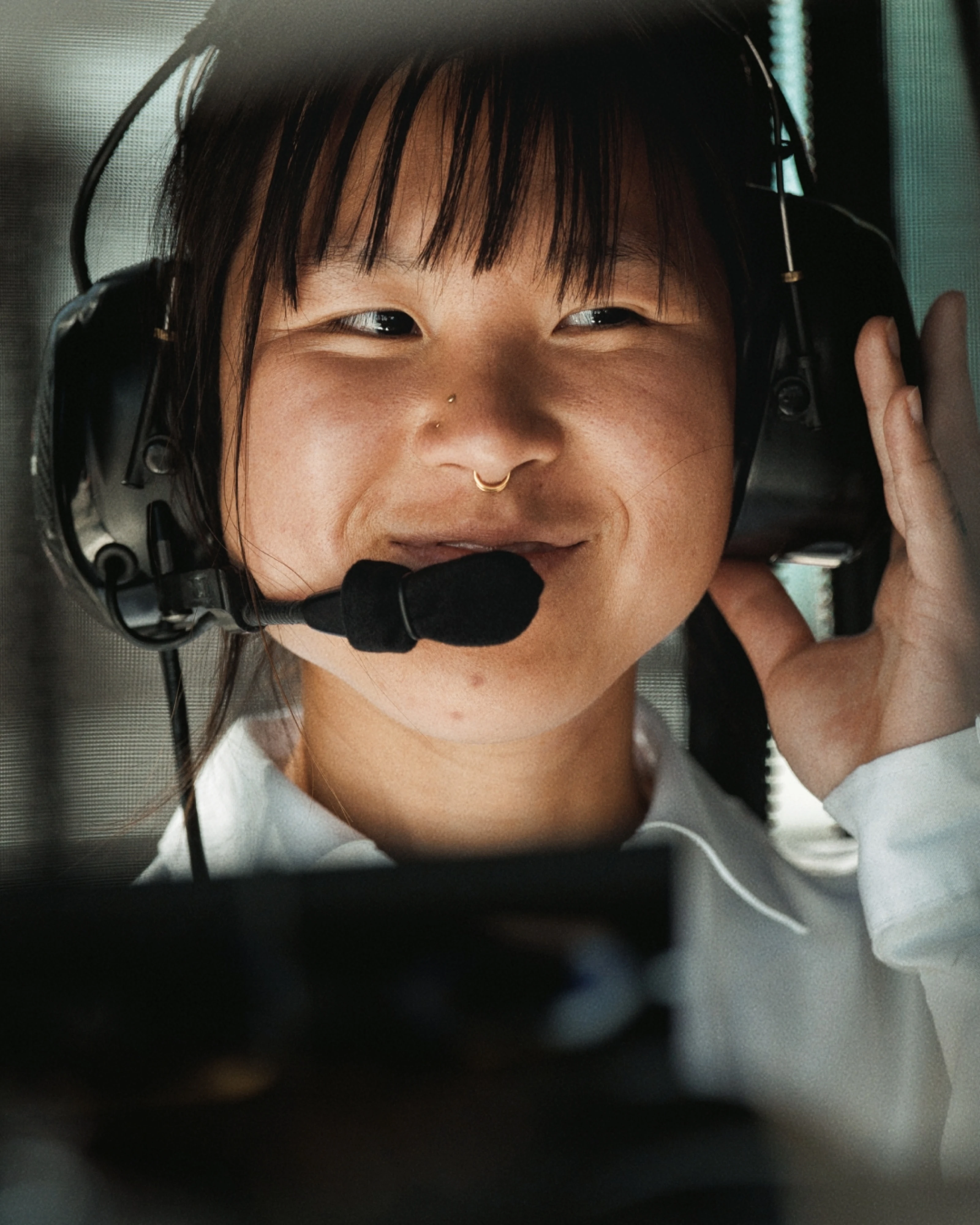 Close-up of a young person smiling and wearing a headset with a microphone, adjusting the earpiece with their hand.