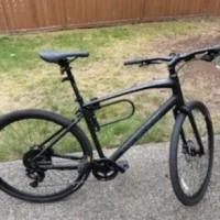 A side-profile of a black bicycle in a fenced yard.