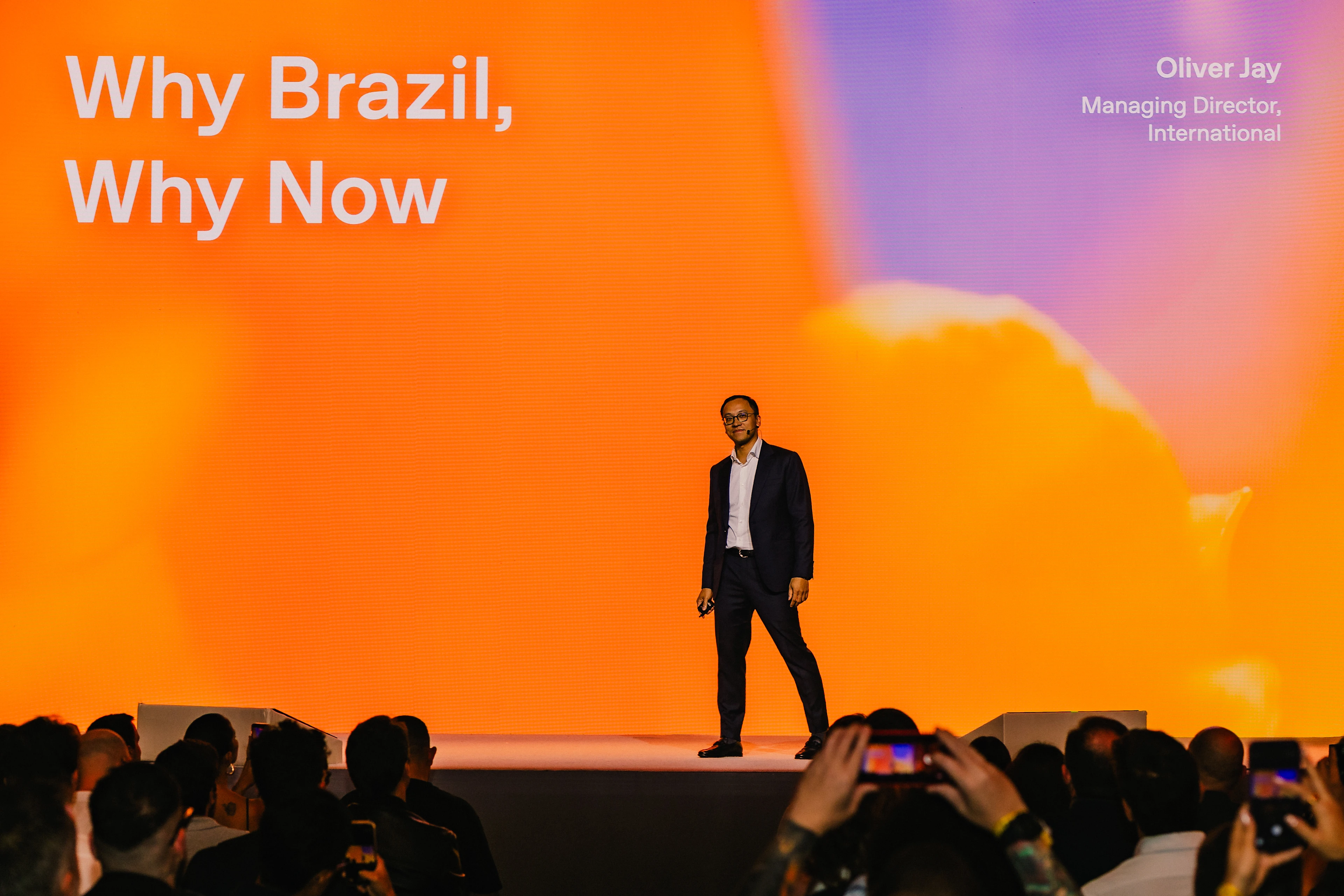 Oliver Jay stands onstage in front of a slide that reads Why Brazil, Why Now.