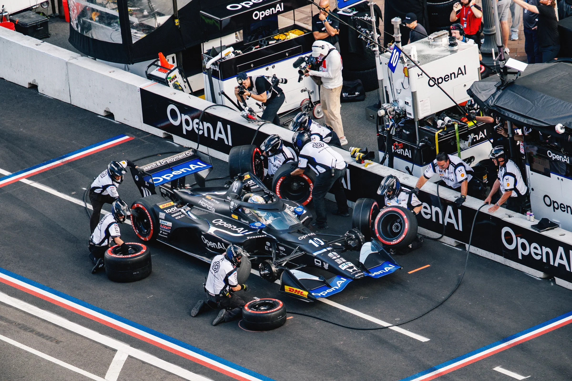 An OpenAI-branded IndyCar and pit crew during a pit stop.