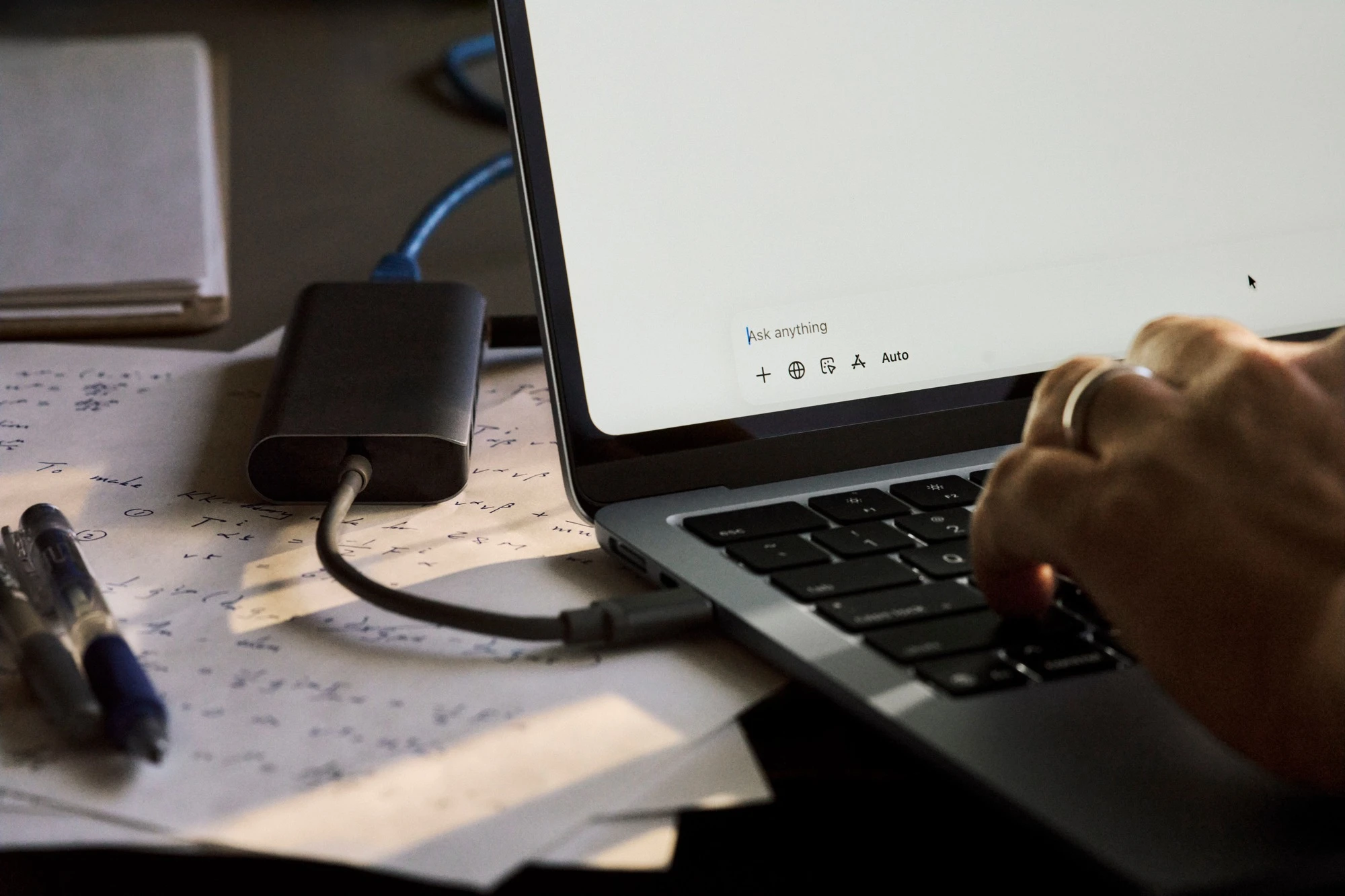 A laptop running ChatGPT beside handwritten notes and an external drive.