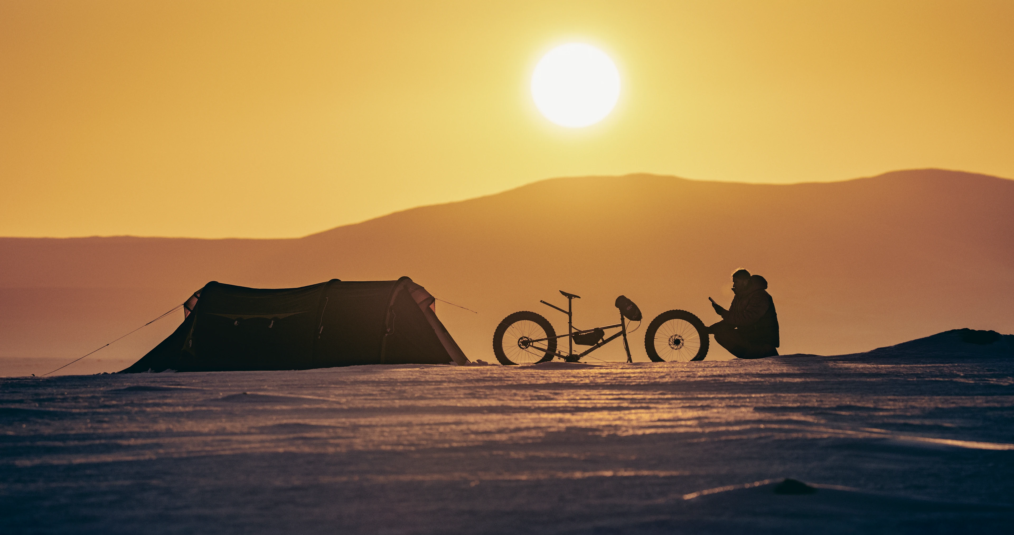 James settles into camp beside his bike and tent at sunset.
