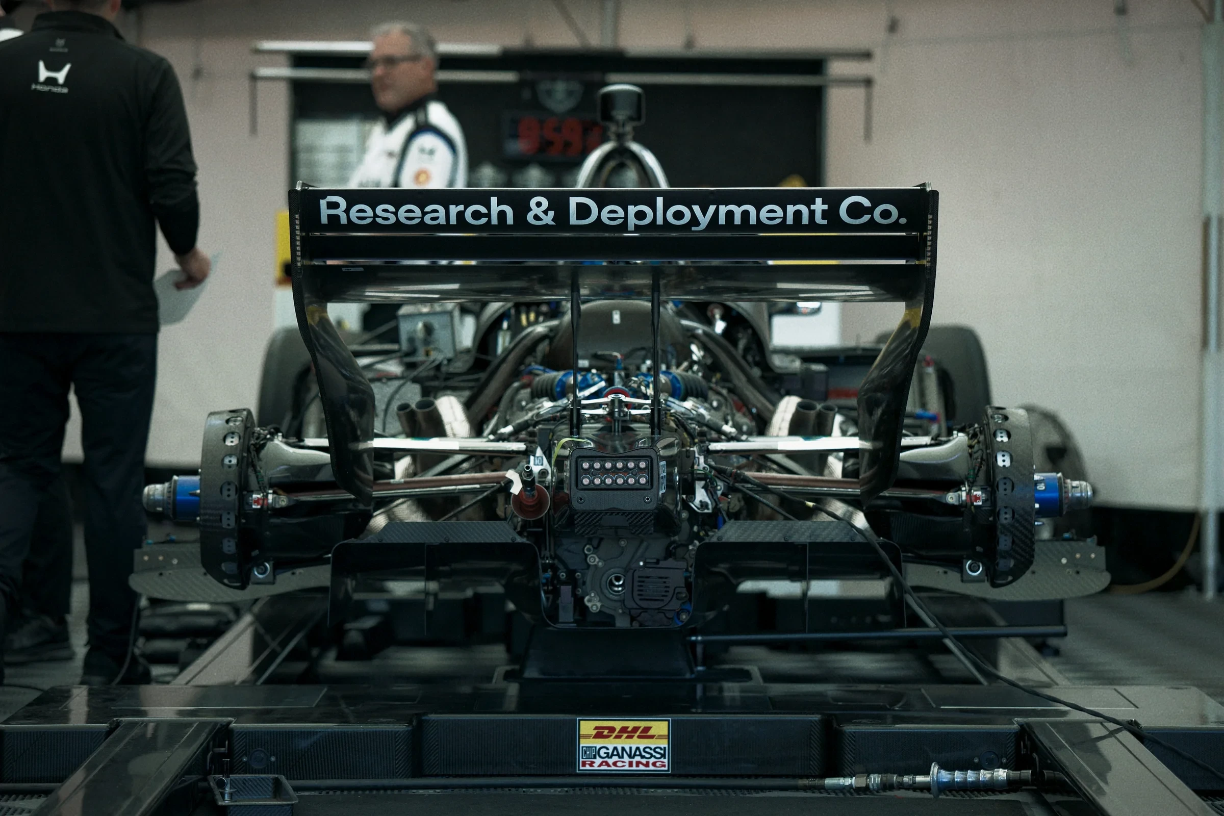 Rear view of an IndyCar in a garage, with Research & Deployment Co. on its rear wing.