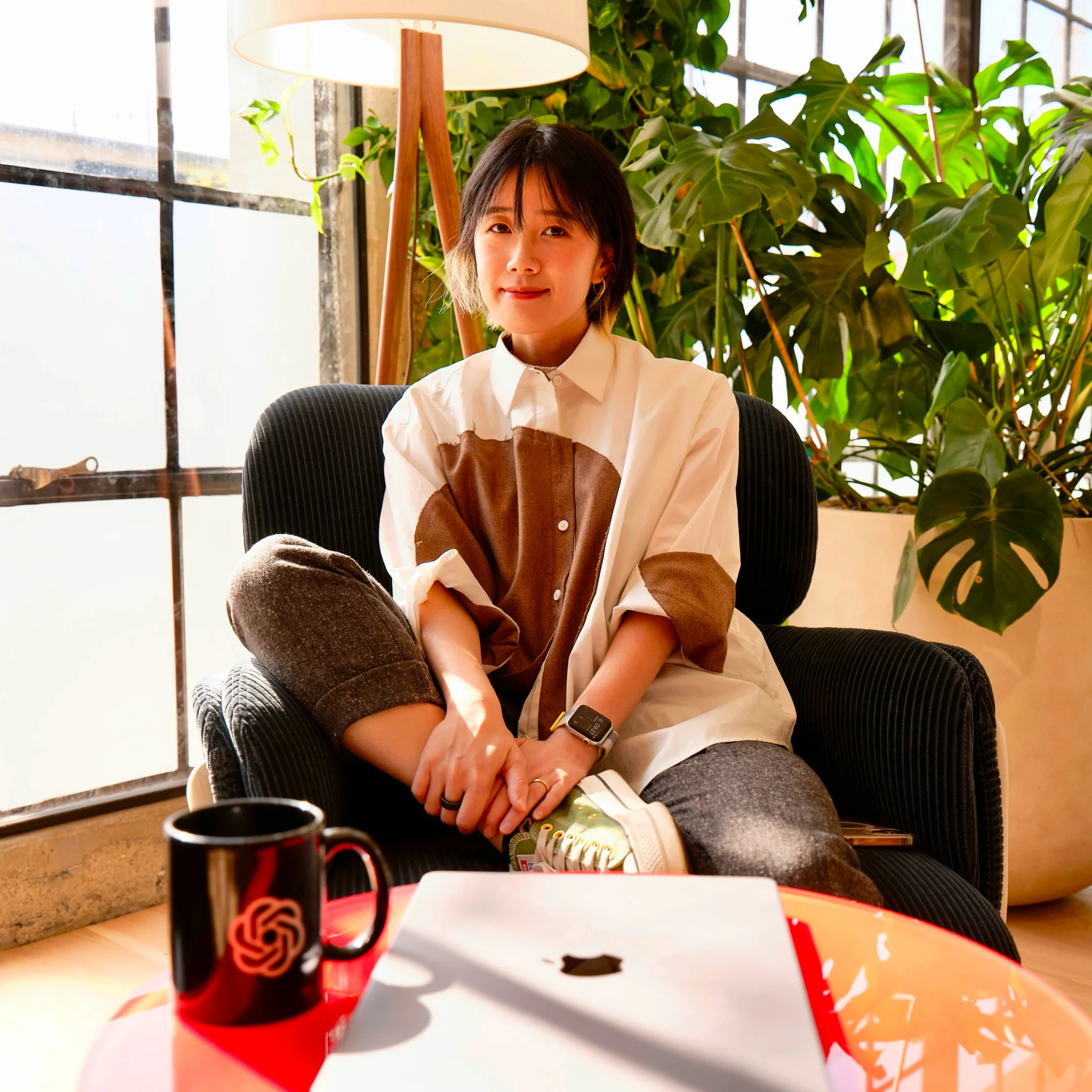 Person sitting on a couch in front of a red coffee table in a plant-filled room