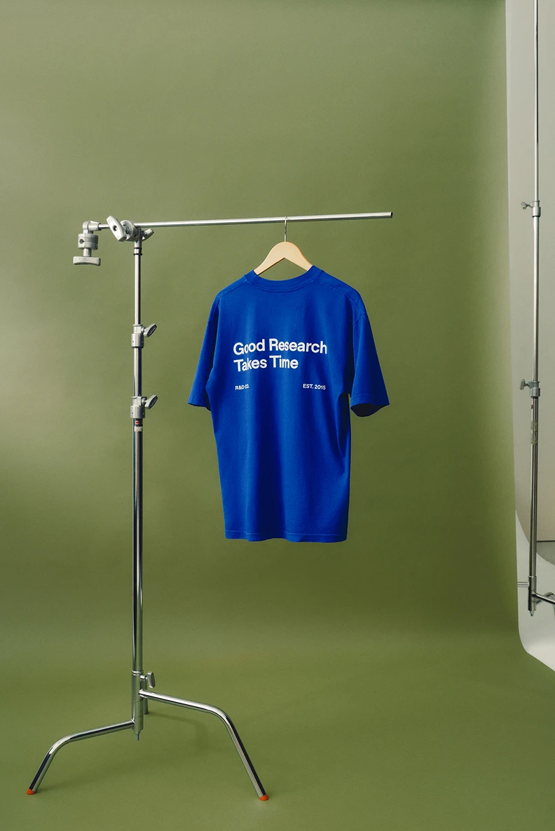 Blue Good Research Takes Time T-shirt hanging on a studio stand