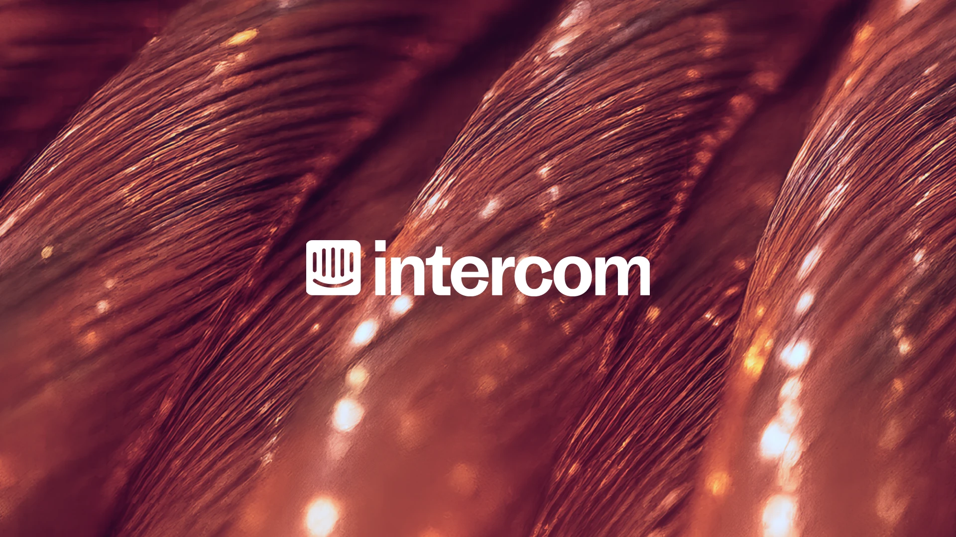 Close-up of copper wire strands with glowing reflections, overlaid with the white Intercom logo centered in the frame.