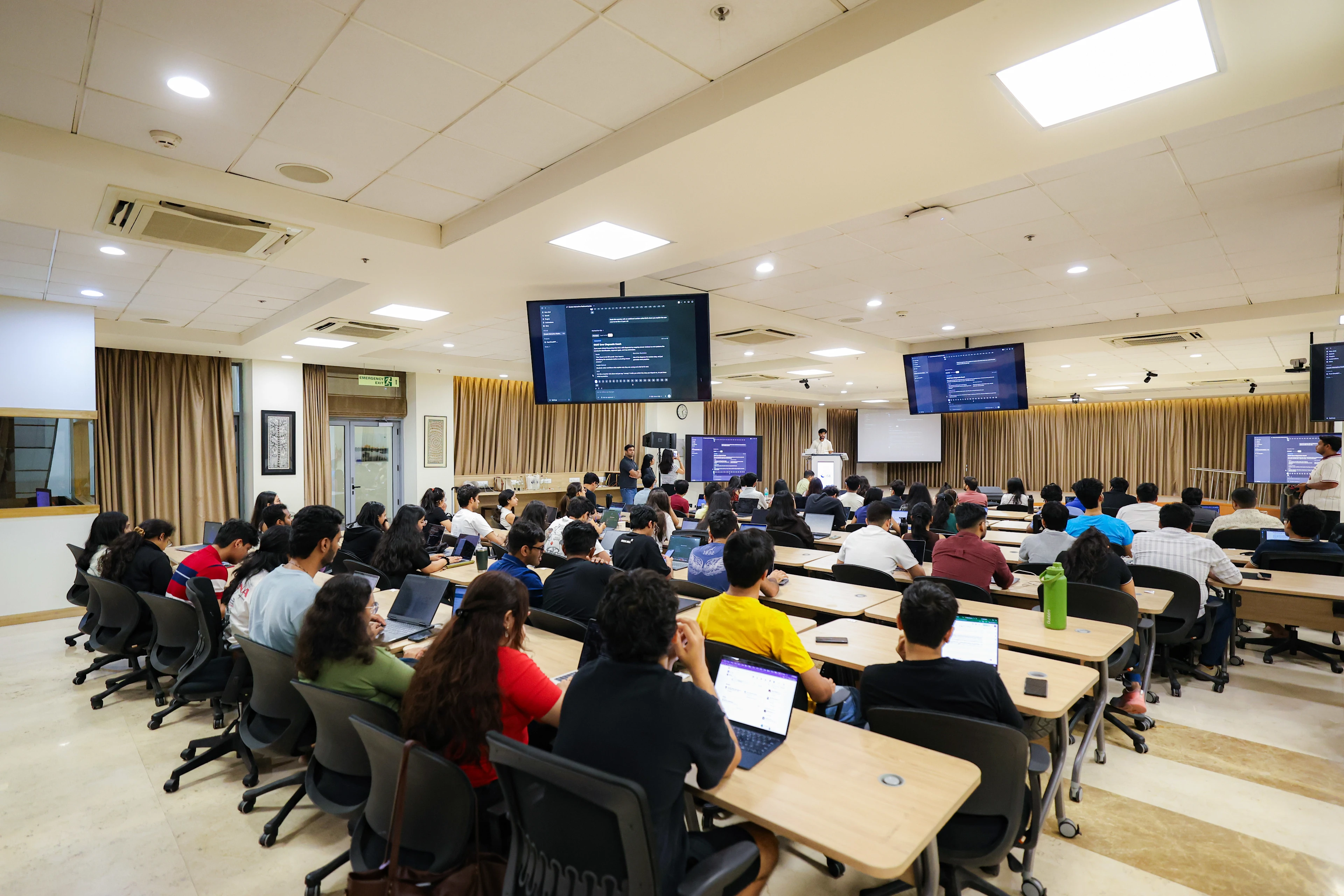Students raising their hands during an AI workshop in a university lecture hall.