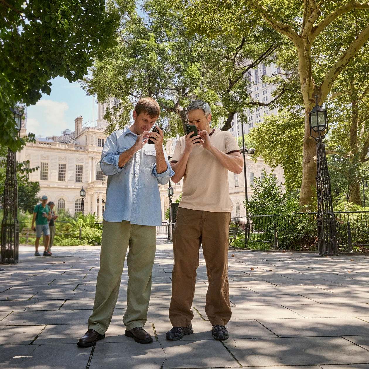 Bradford and Bryan Manning use their phones while standing in a city park.