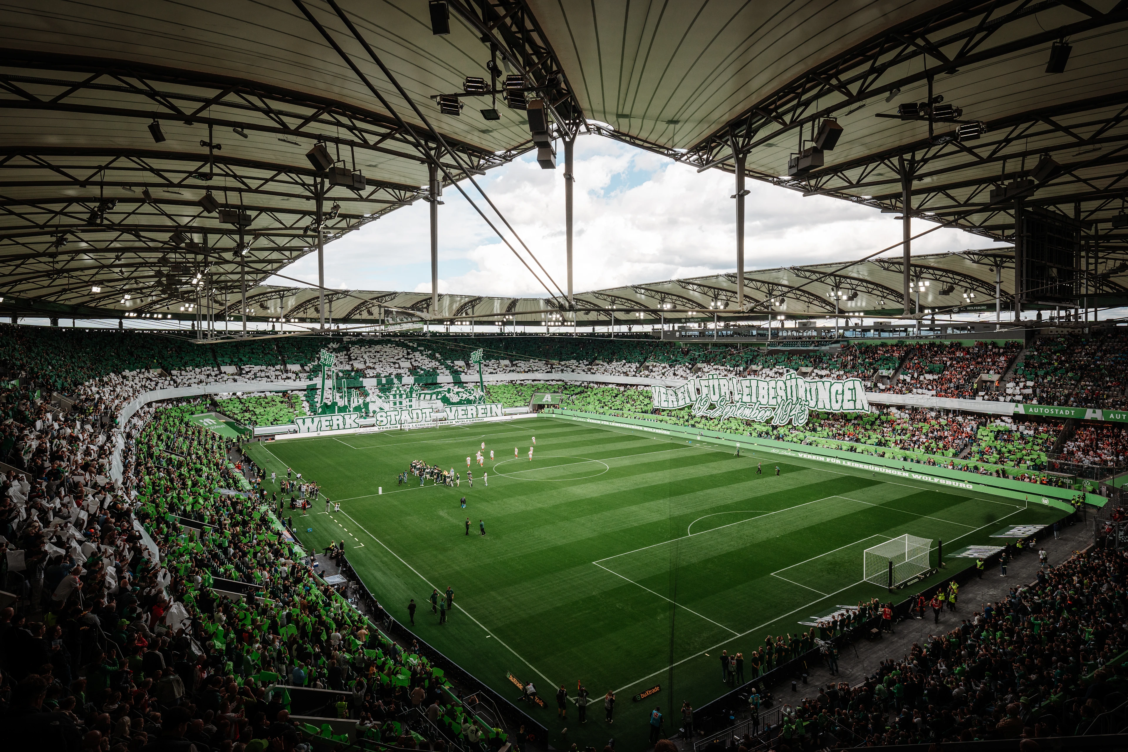 Panoramic view of VfL Wolfsburg’s home stadium filled with green-and-white supporters, displaying a large coordinated tifo across the stands.