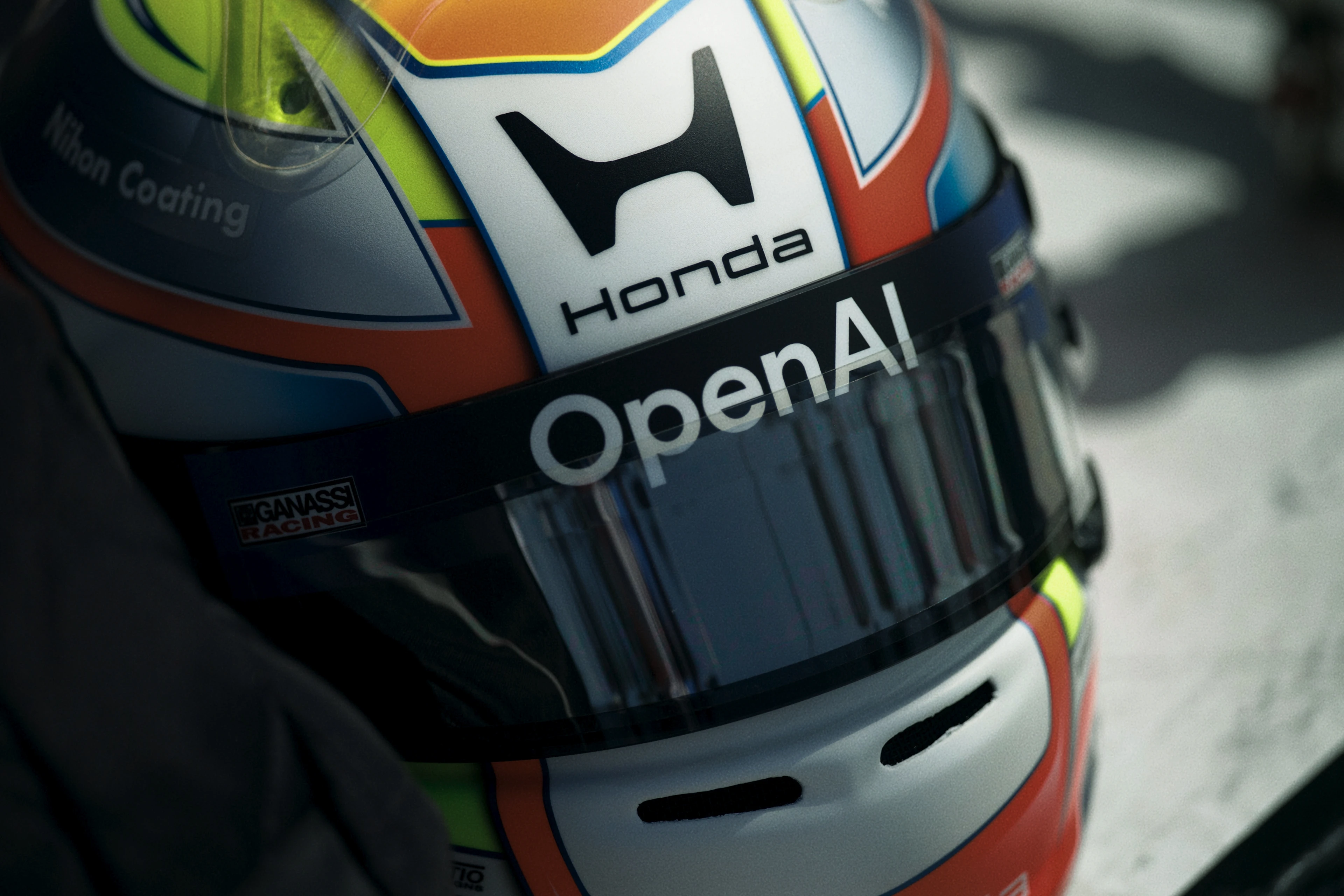 Close-up image of a racing helmet with a colorful design featuring logos of Honda, OpenAI, and Chip Ganassi Racing on the visor and shell.