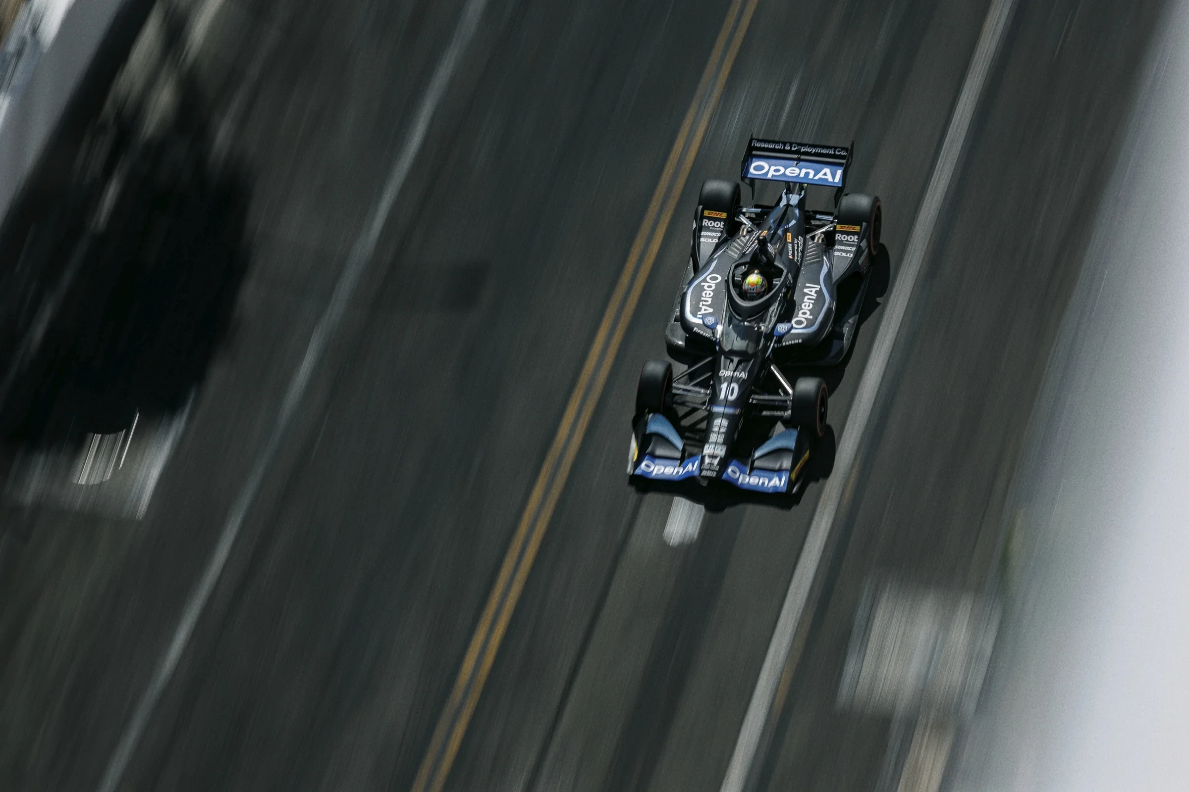 Overhead view of an OpenAI-branded IndyCar speeding along the track.