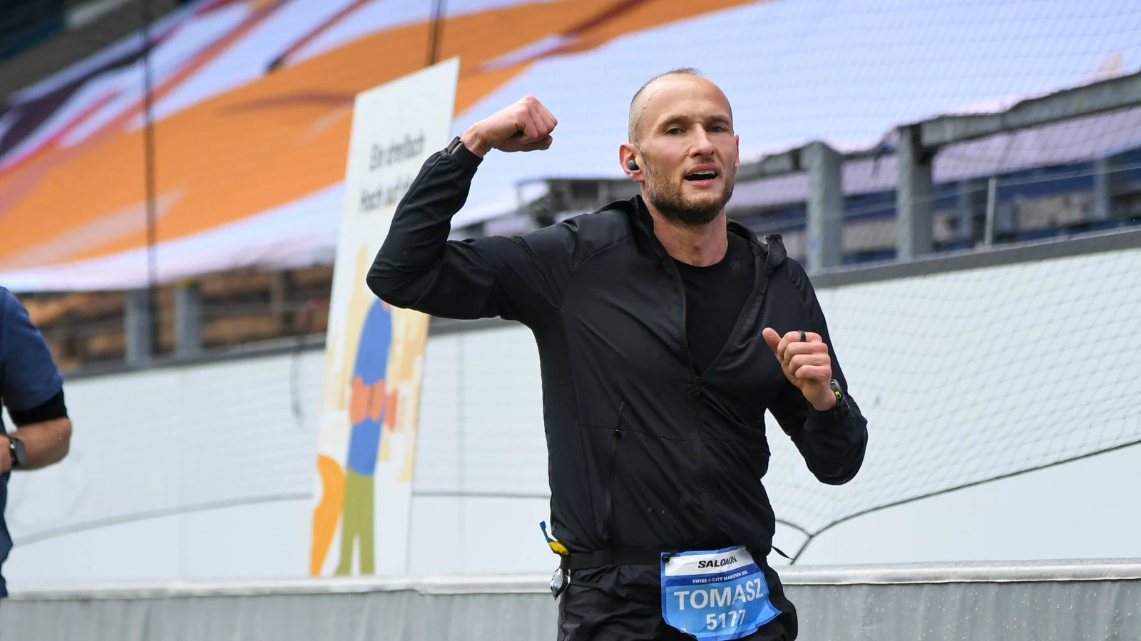 Tom Tomaszewski running in a race with one arm raised.