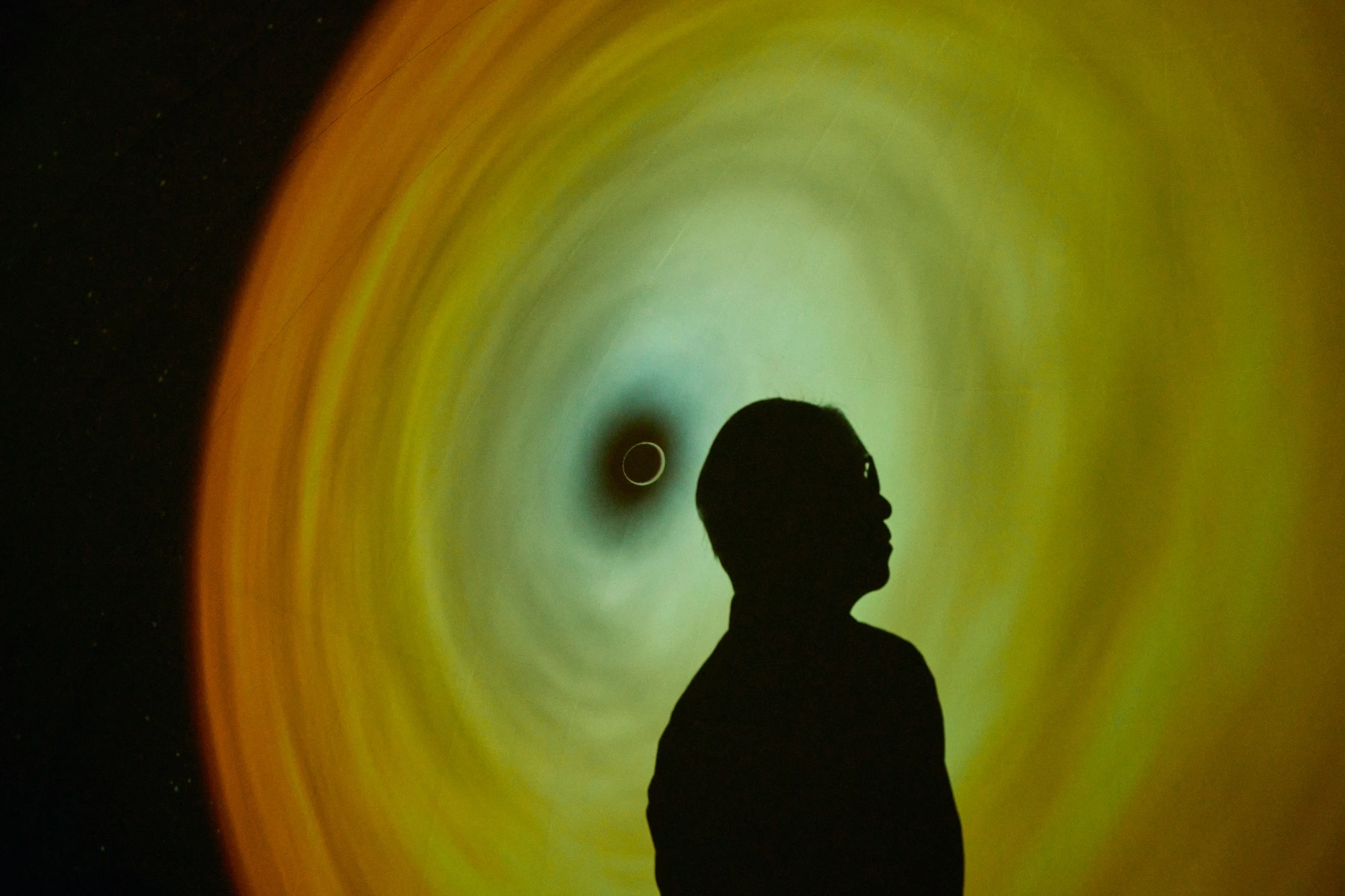 A silhouette stands in front of a simulated black hole visualization.