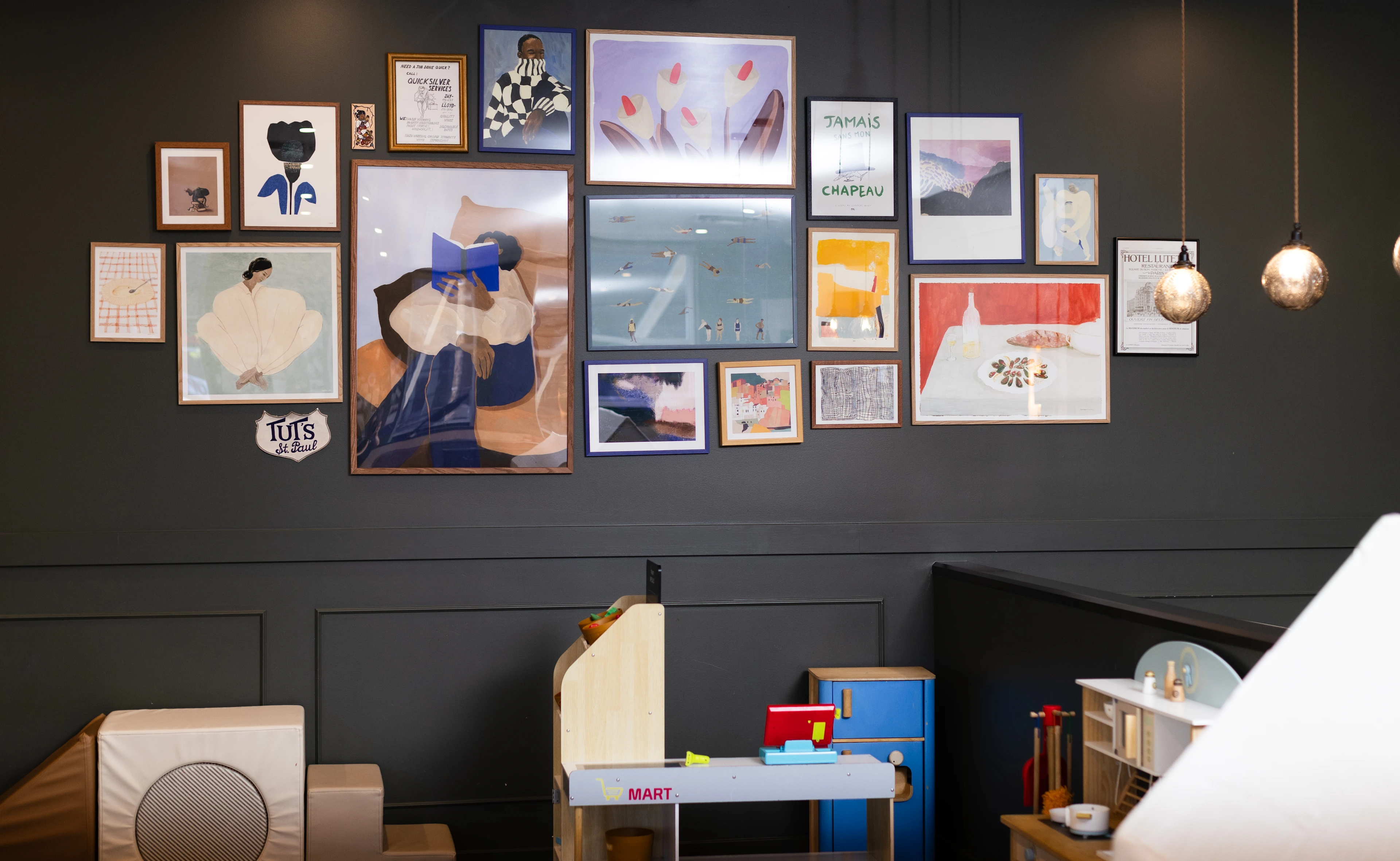 A framed art wall and children's play area inside The Den Family Social.