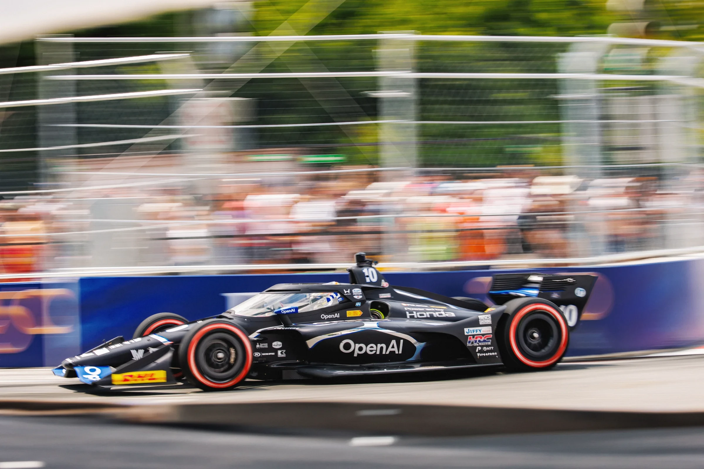 An OpenAI-branded IndyCar speeds past spectators.