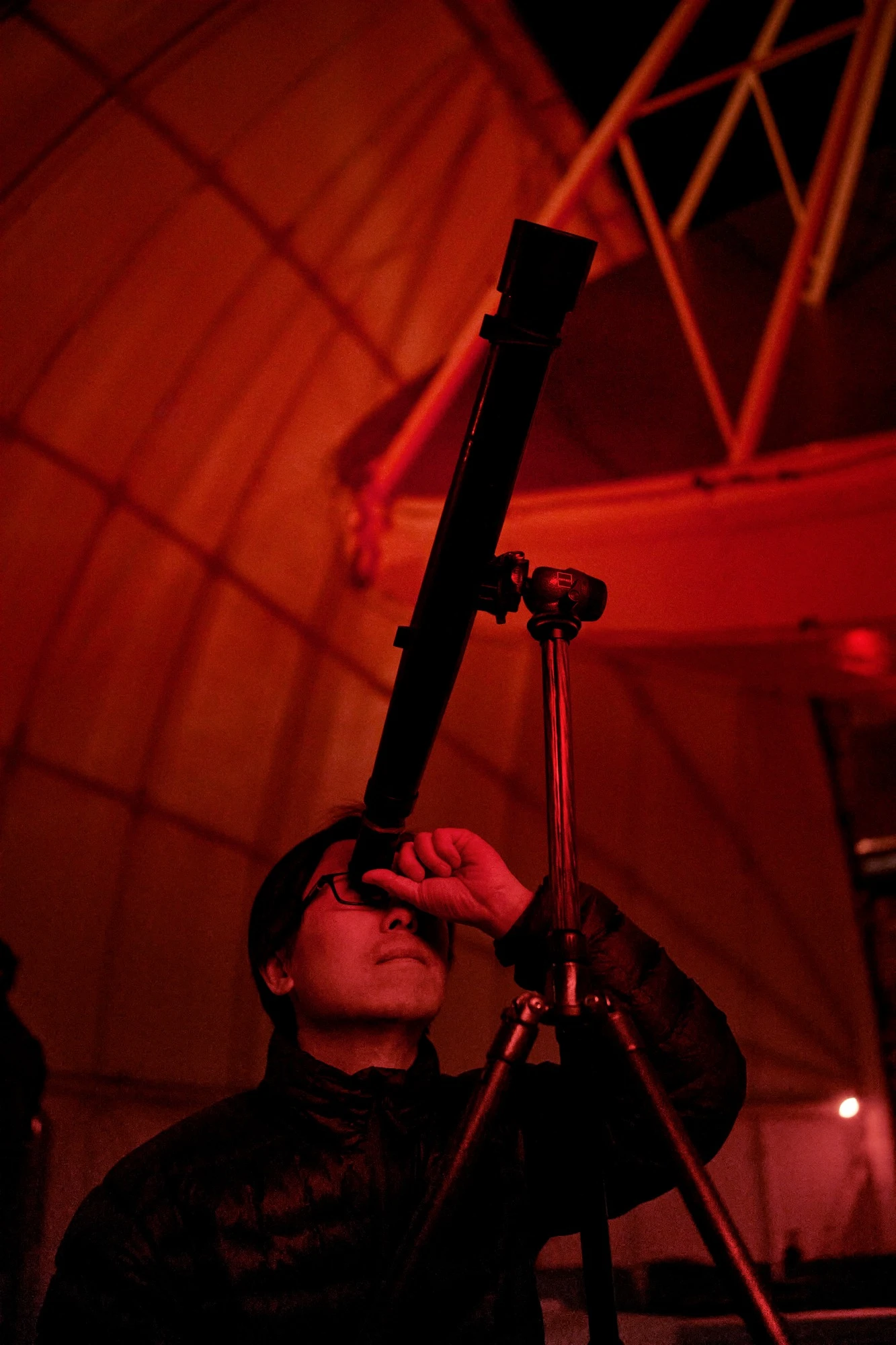 CK Chan looks through a telescope in red observatory light.