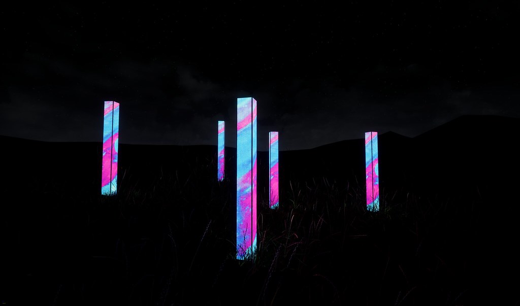 Four illuminated columns stand in a field at night