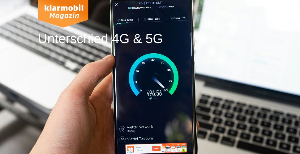 Person hält Handy, auf dem Speedtest durchgeführt wird in der Hand, im Hintergrund verschwommen zwei Laptops