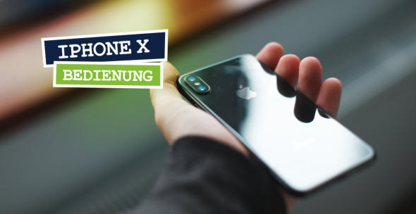 Ein iPhone X wird in der Hand gehalten mit dem Display nach unten und dem Logo nach oben.