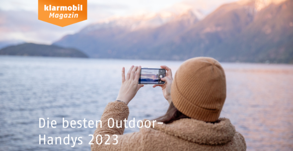 Frau macht Foto von See in den Bergen. Aufschrift: Die besten Outdoor-Handys 2023