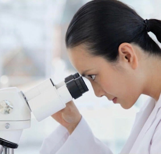 Healthcare professional in a lab coat examining through a microscope