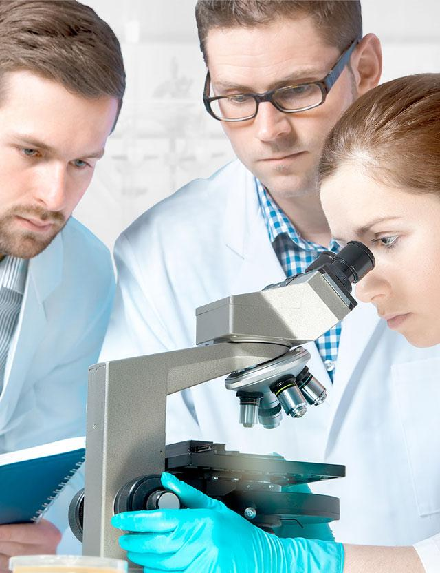 Three healthcare professional in lab coats huddled around a microscope, collaborating on an examination