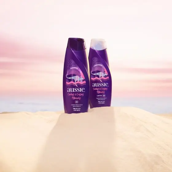 Frascos de Aussie Shampoo e condicionador Cachos & Crespos ativados com fundo lilás.