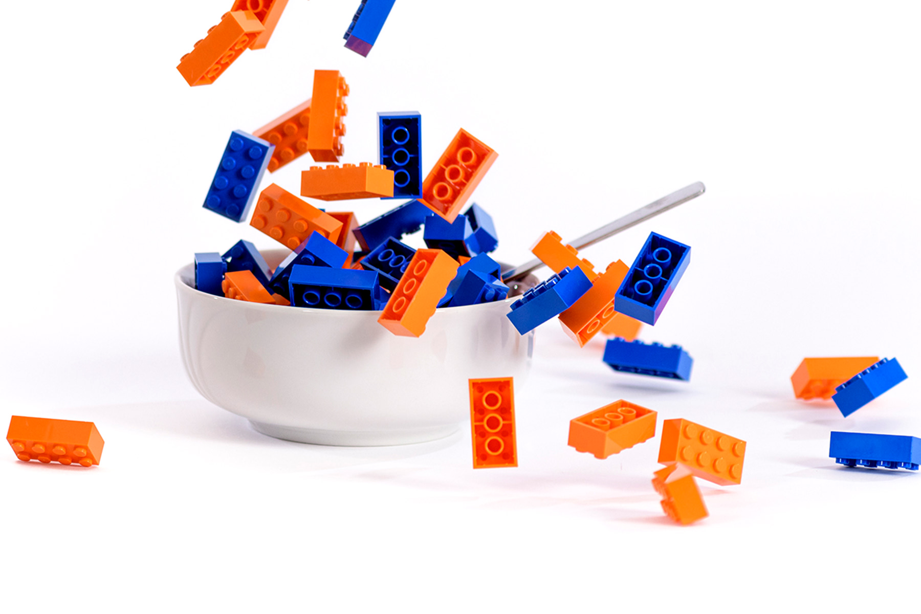 Blauw en oranje lego blokjes in een witte schaal met een lepel