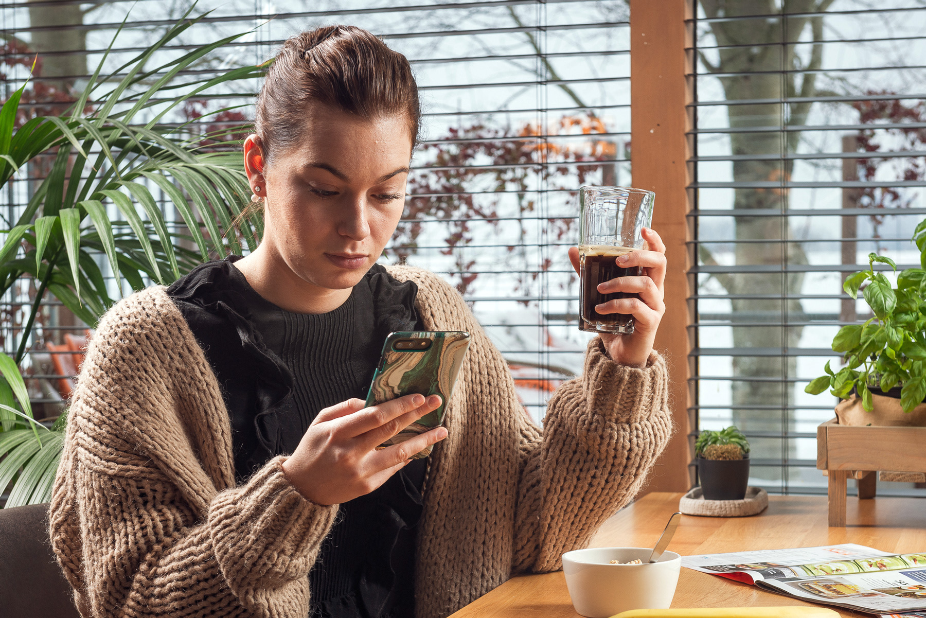 vrouw aan tafel met mobiel en koffie in hand