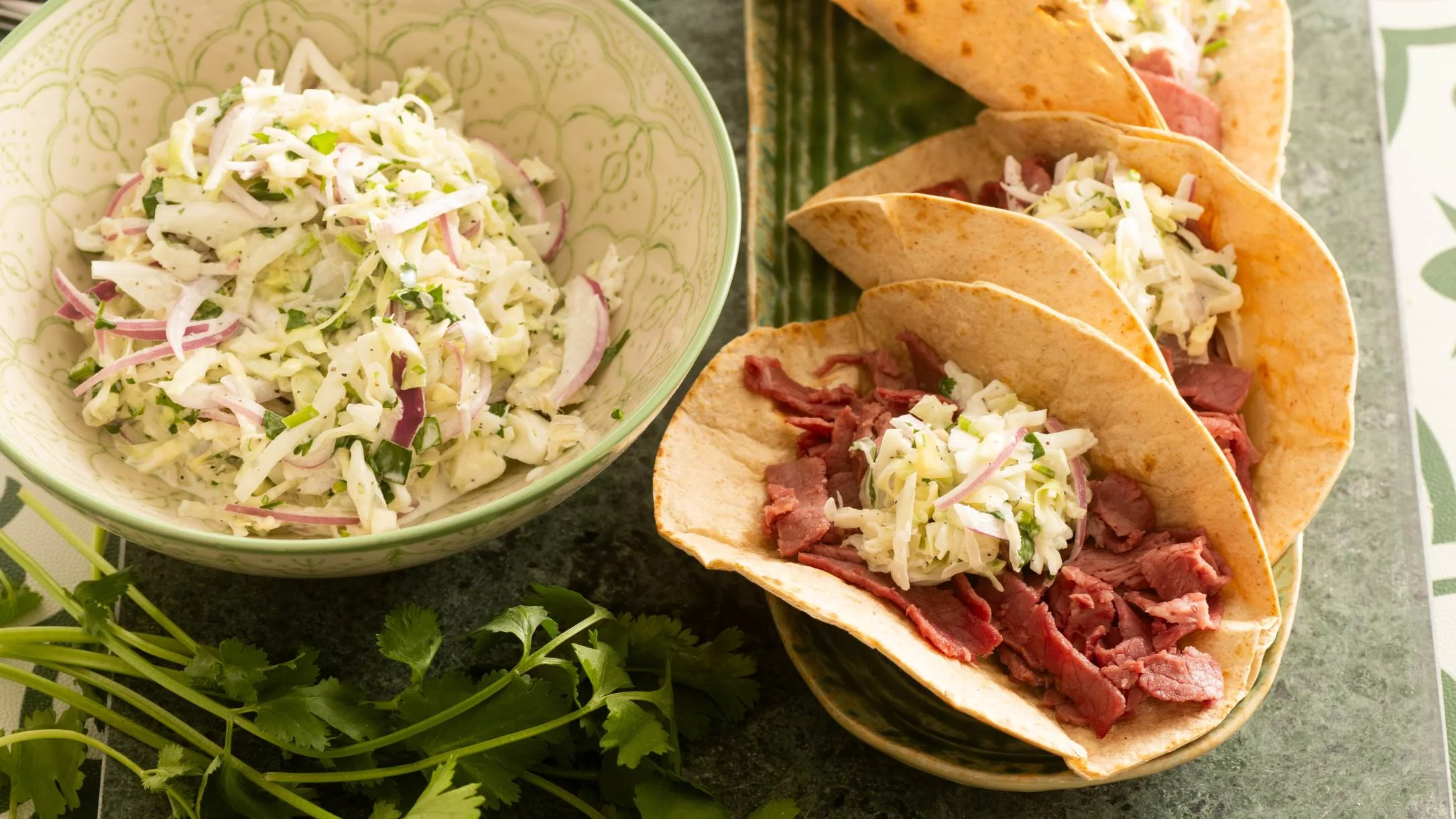 Beef tacos with fresh cabbage slaw in a green bowl, garnished with cilantro on a stone countertop.