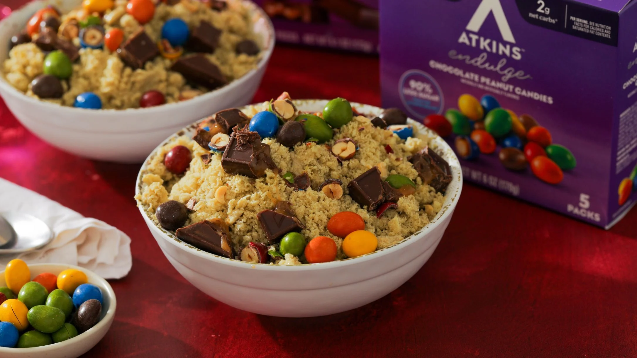 Two white bowls of shredded ice topped with colorful candies and chocolate chunks, next to an Atkins Endulge Chocolate Peanut Candies box.