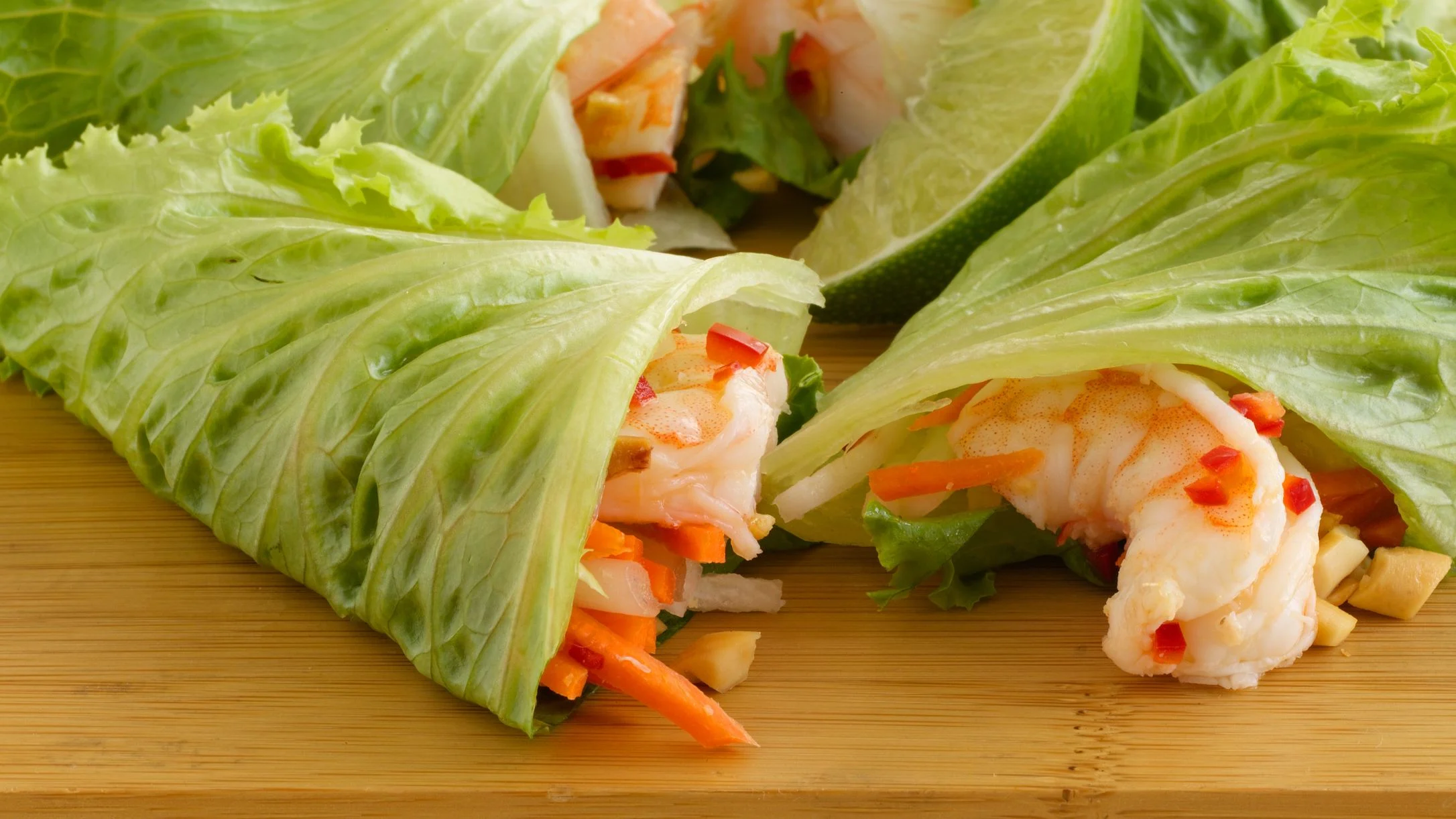 Fresh lettuce wraps filled with shrimp, carrots, and red peppers on a wooden cutting board.