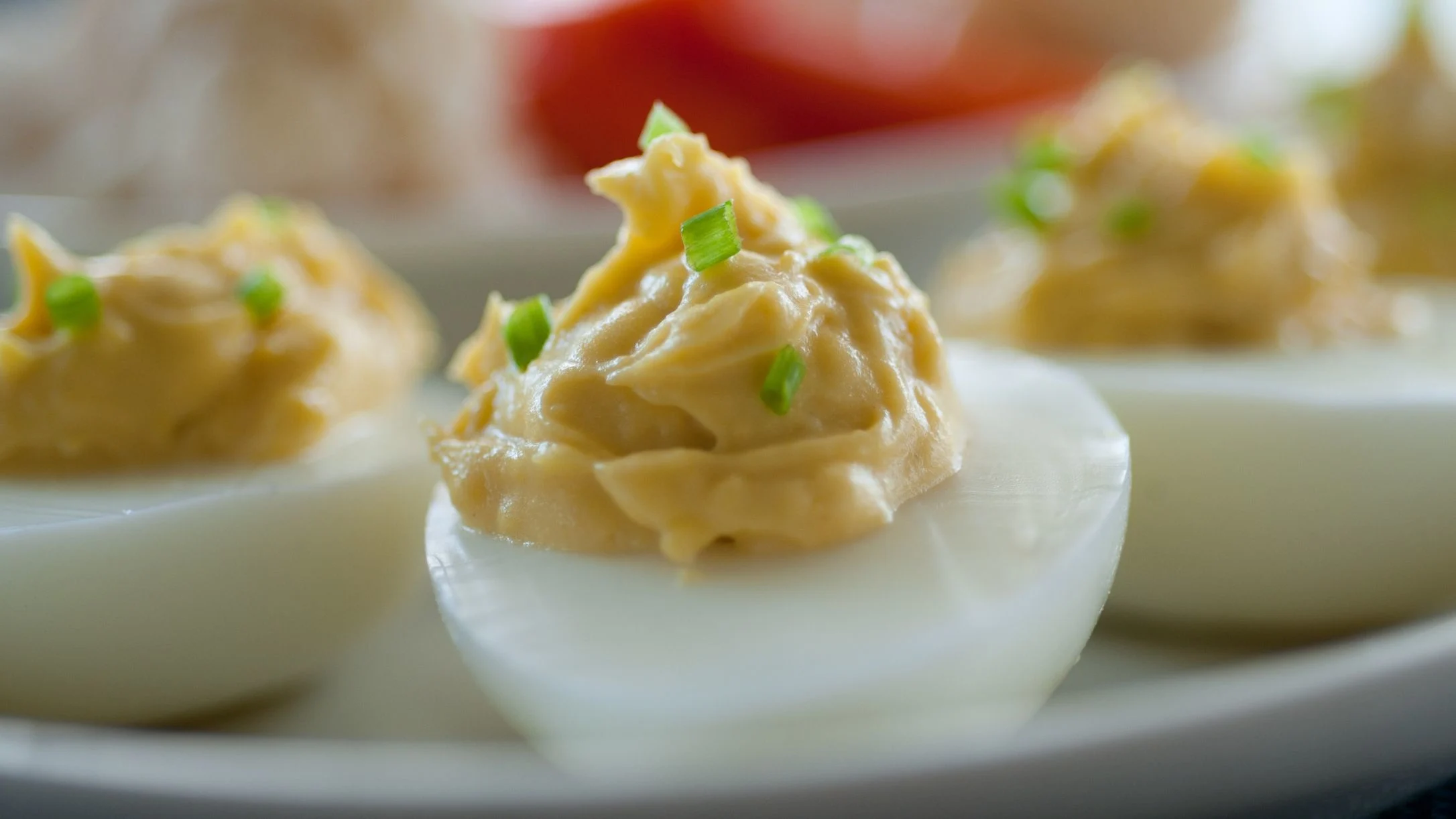 Deviled eggs topped with creamy yellow yolk filling and chopped green chives, arranged on a white plate.