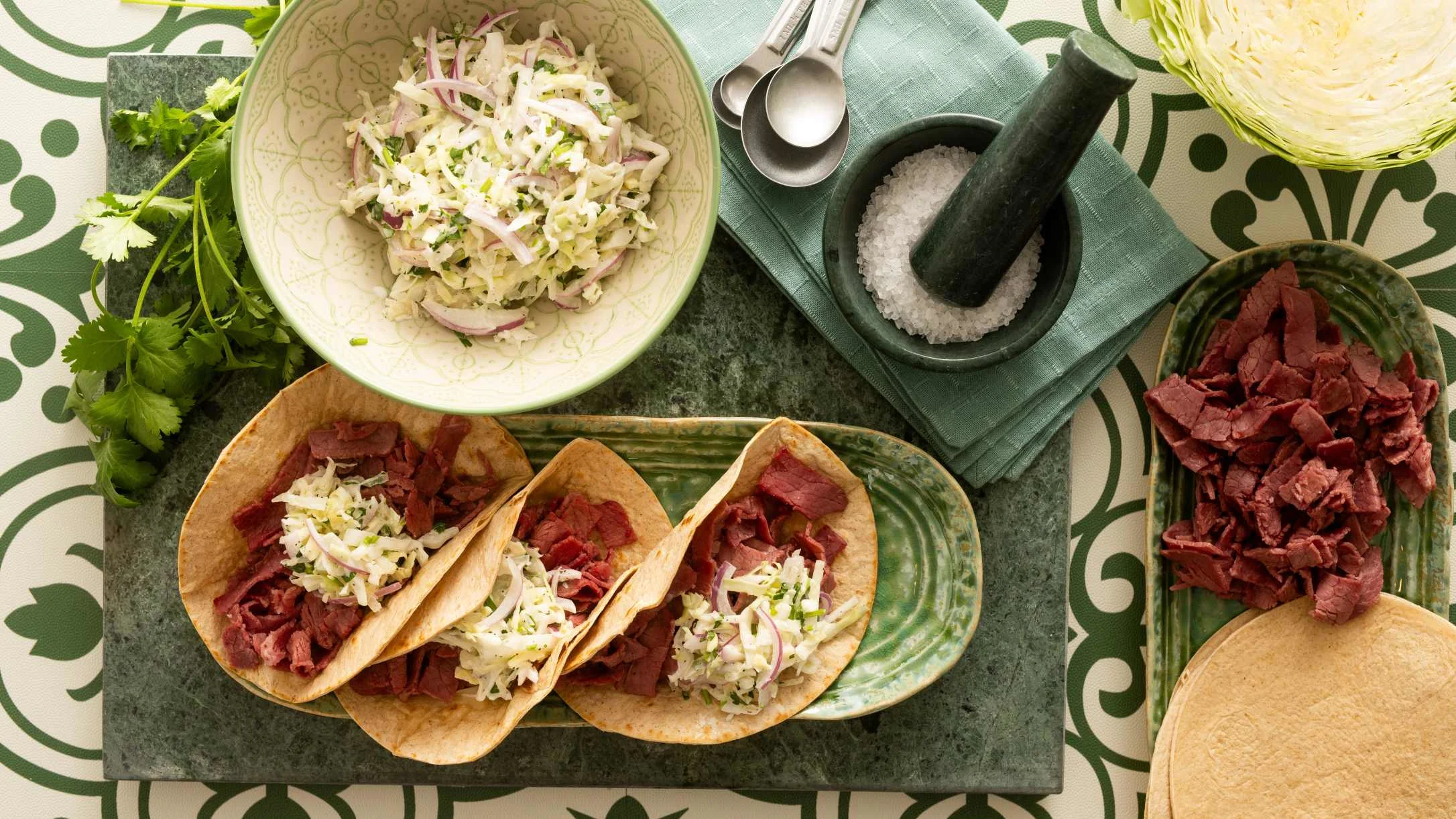 Beef tacos with cabbage slaw, served with mortar of salt, fresh cilantro, and additional meat and slaw in bowls.