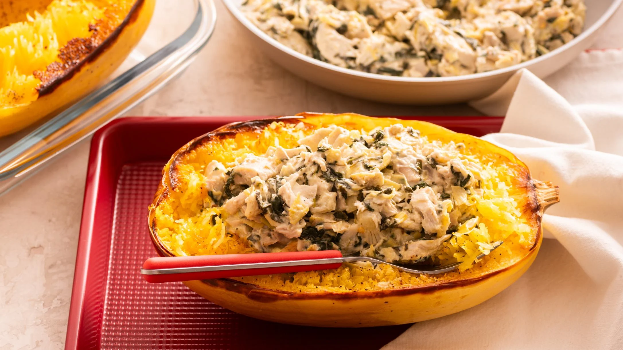 Roasted spaghetti squash filled with creamy chicken and spinach mixture, served on a red tray with extra filling nearby.