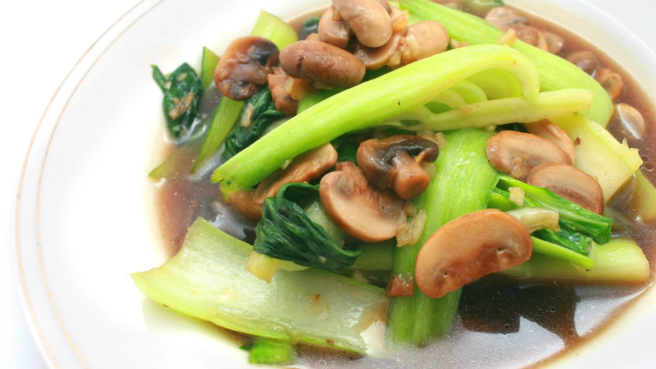 A white plate with stir-fried bok choy and sliced brown mushrooms in a savory brown sauce.