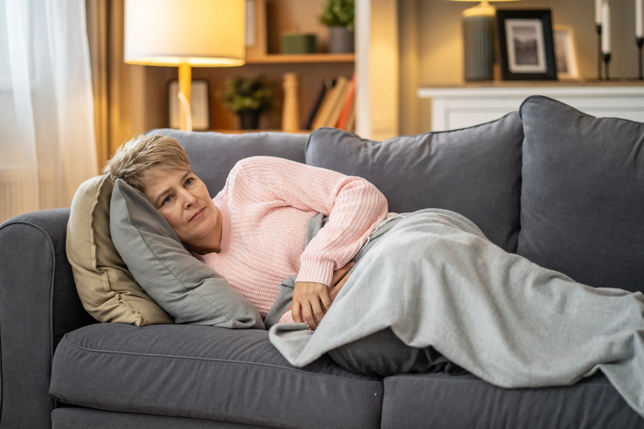 Woman laying in a sofa with a blanket while watching tv