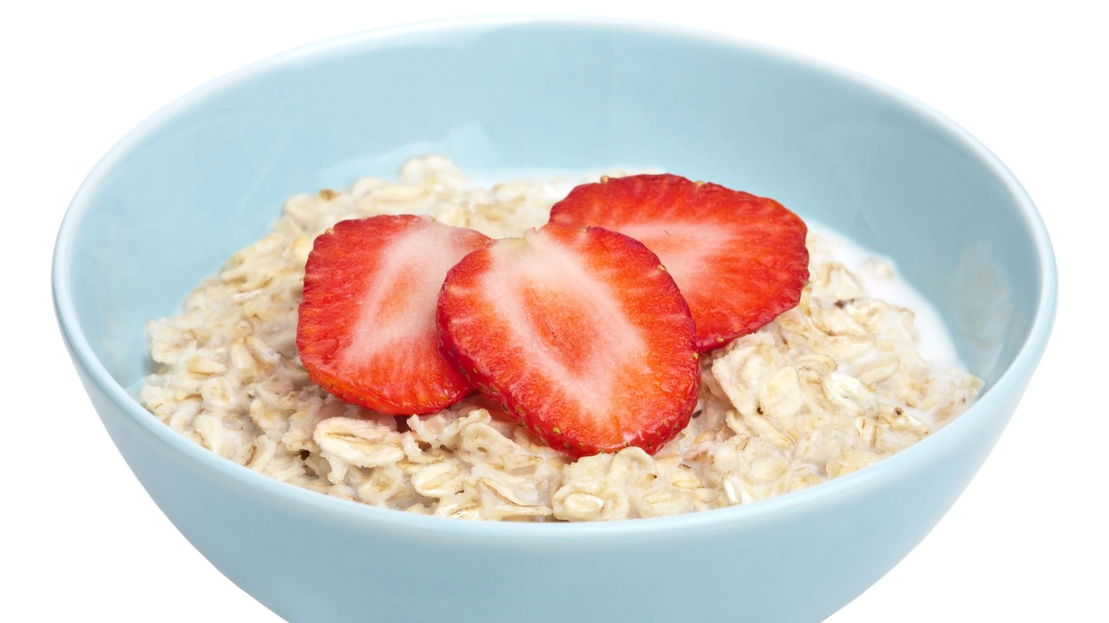A light blue bowl filled with oatmeal topped with three sliced fresh strawberries on a white background.