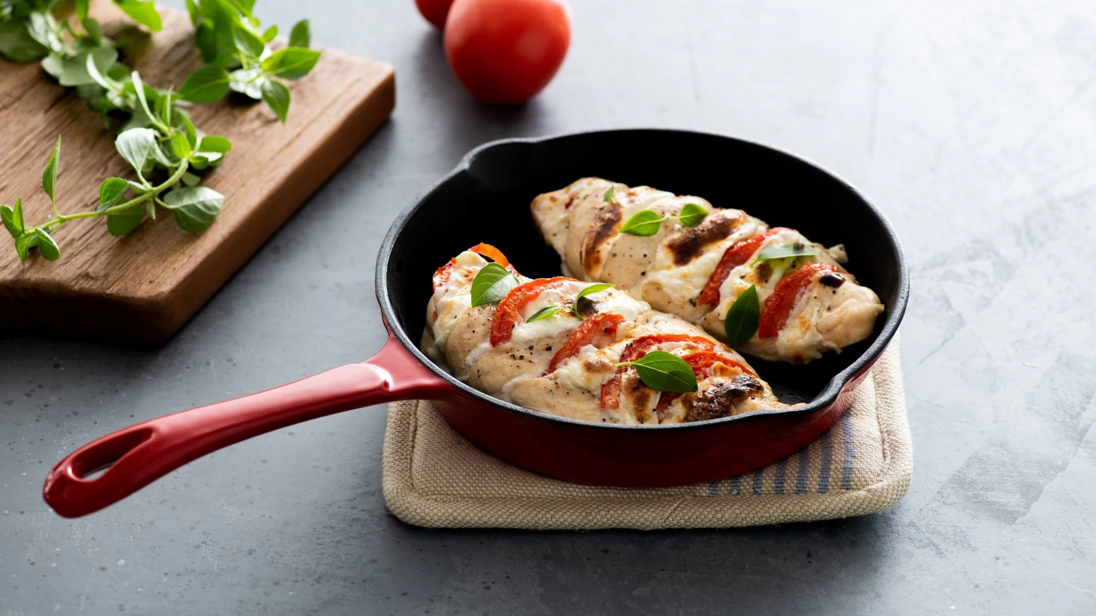 Grilled chicken breasts topped with tomatoes peppers and fresh basil in a red cast iron skillet.