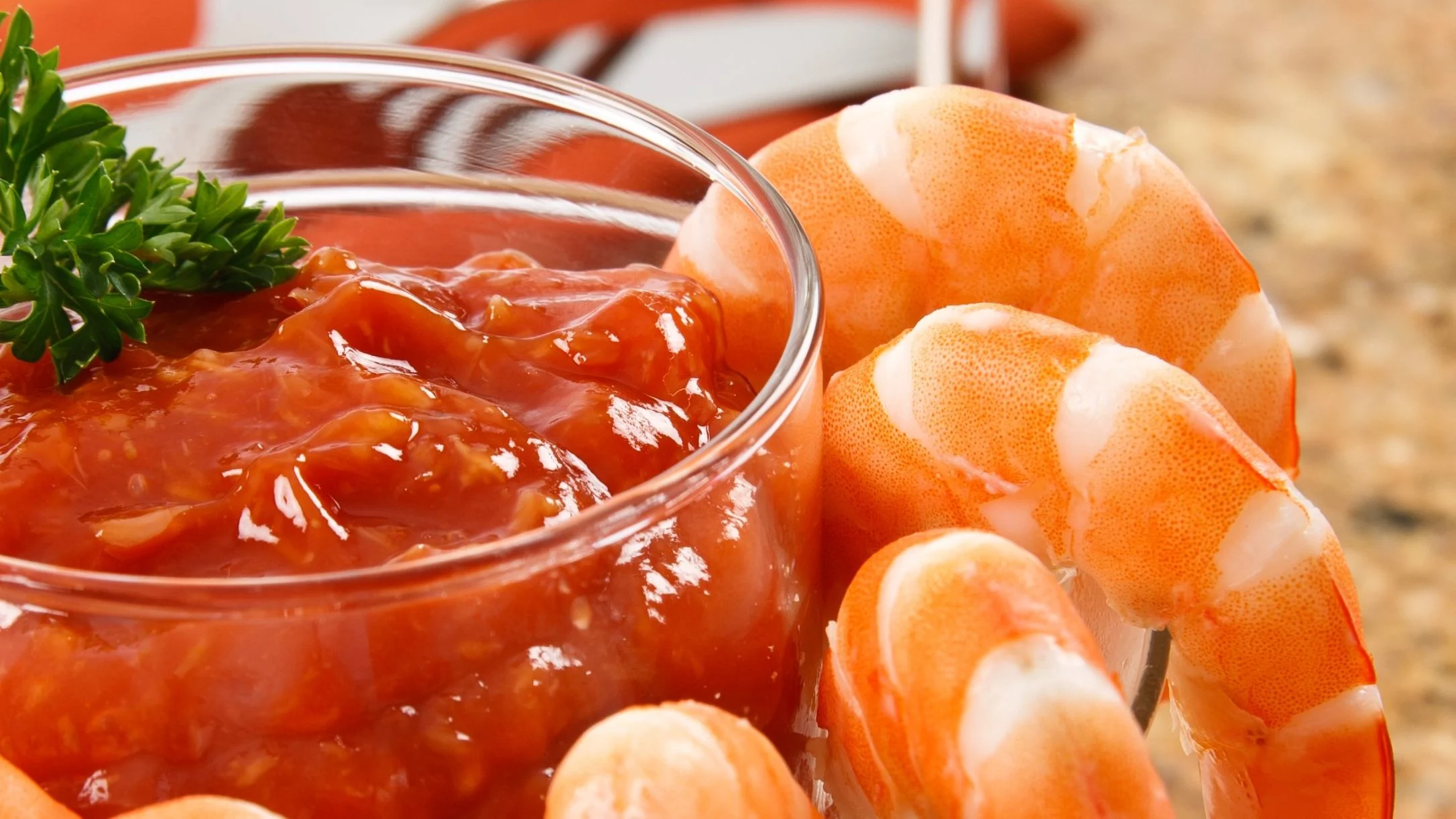 Cooked shrimp arranged around a glass bowl of red cocktail sauce, garnished with fresh parsley.