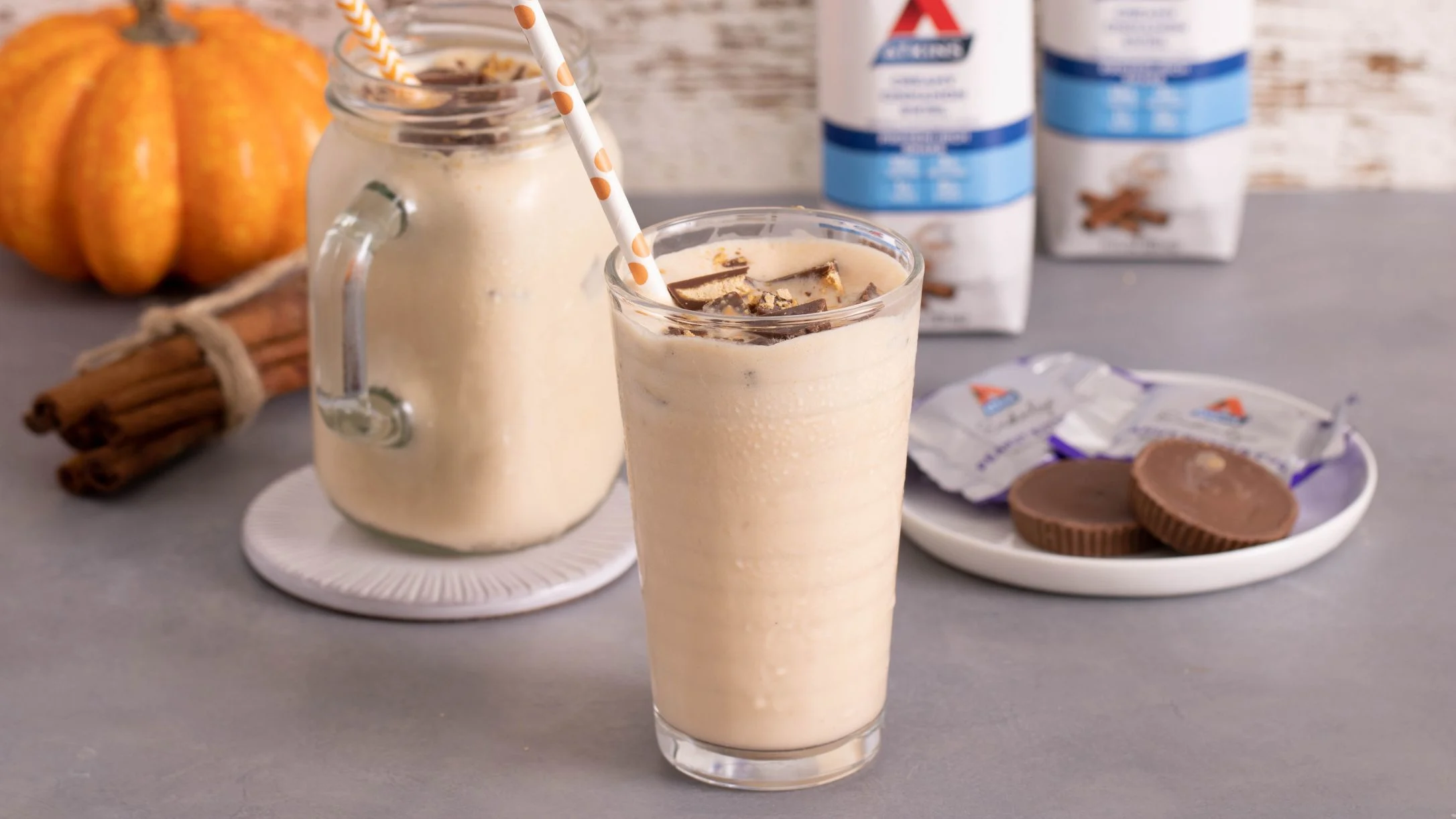 Creamy pumpkin spice milkshakes with striped straws, served alongside chocolate peanut butter cups and cinnamon sticks.