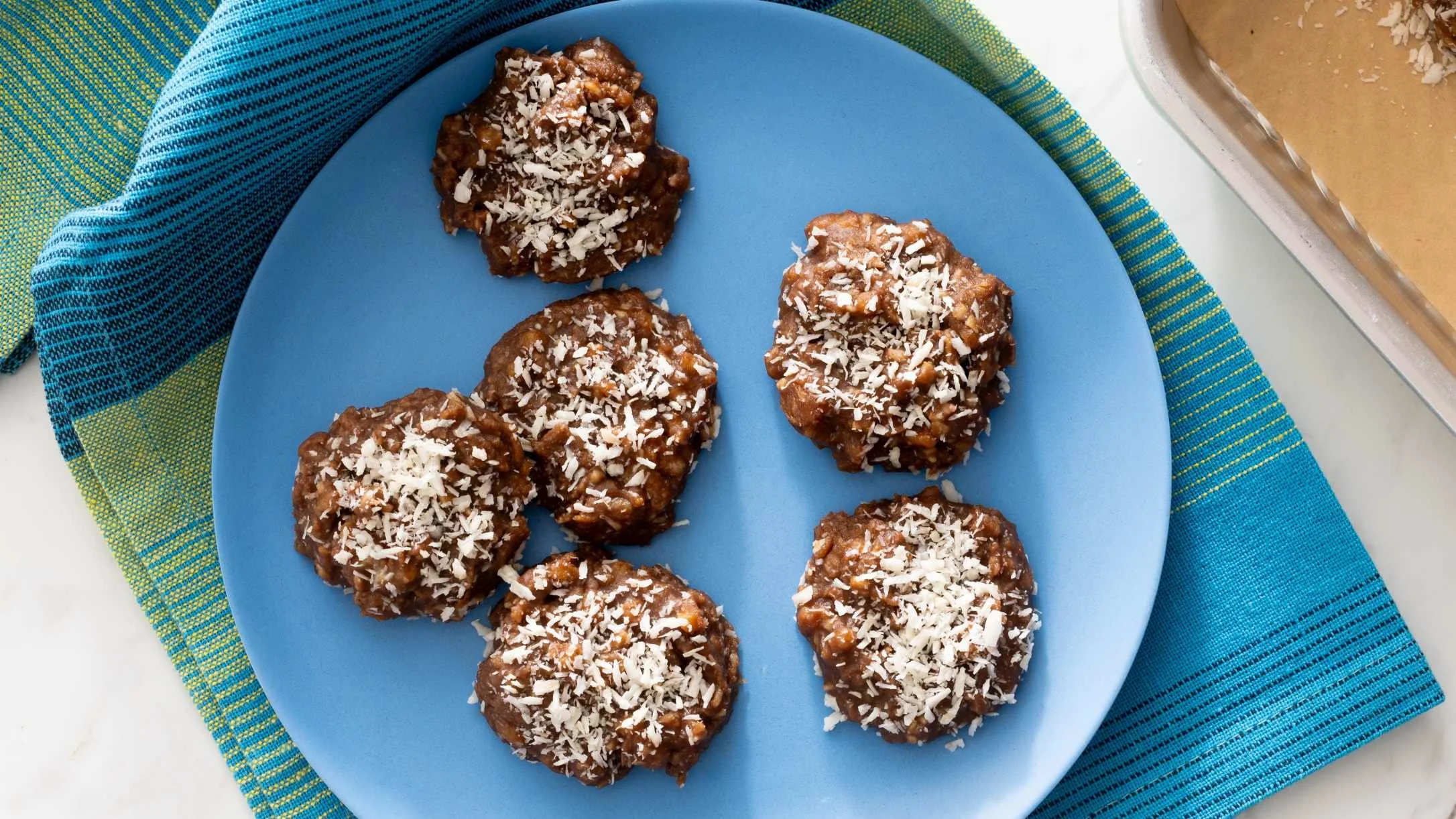 Chocolate coconut cookies arranged on a blue plate, sitting on a turquoise and green striped placemat.