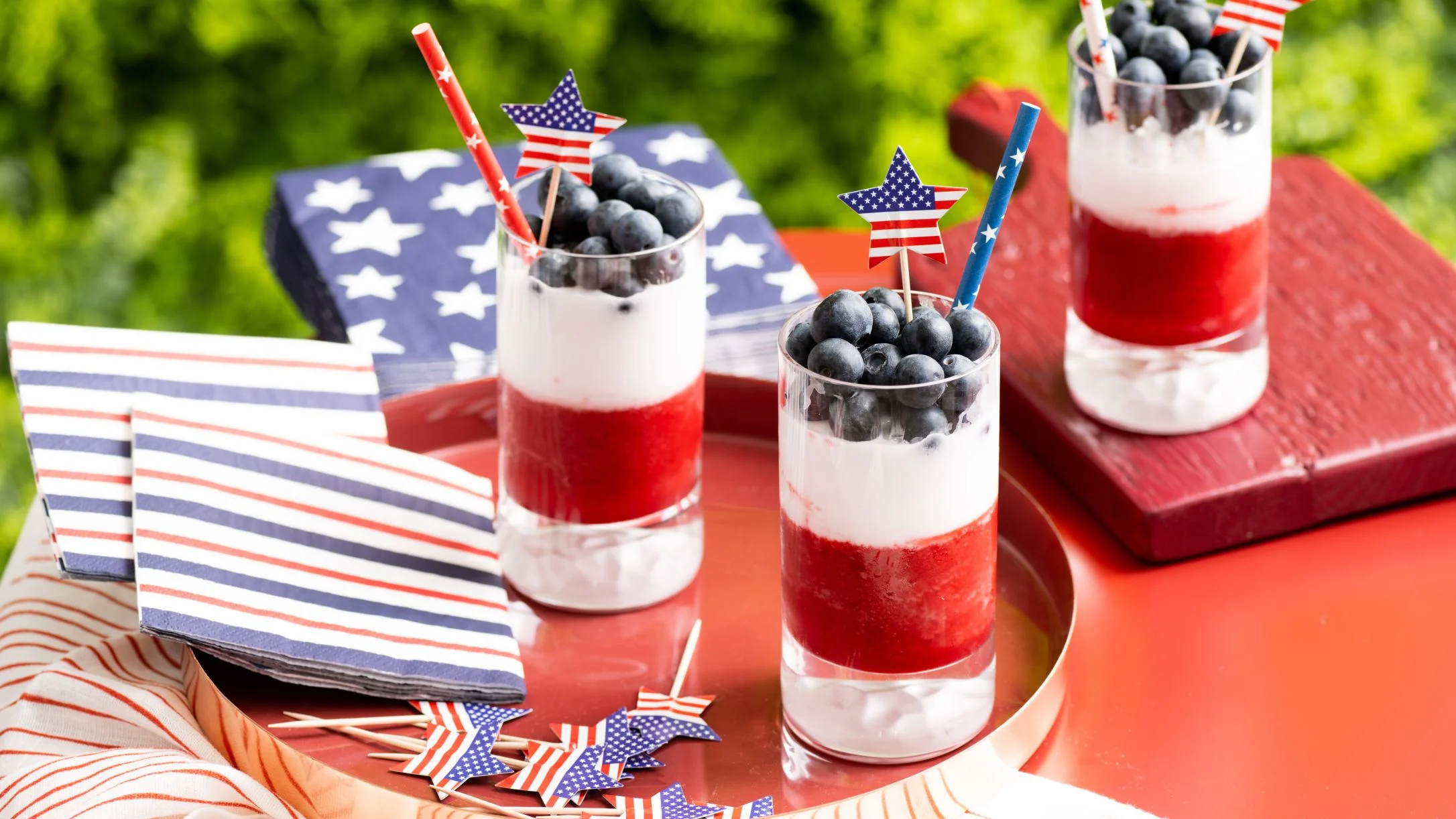 Patriotic red, white, and blue  layered drinks with blueberries and American flag decorations for Fourth of July celebration.