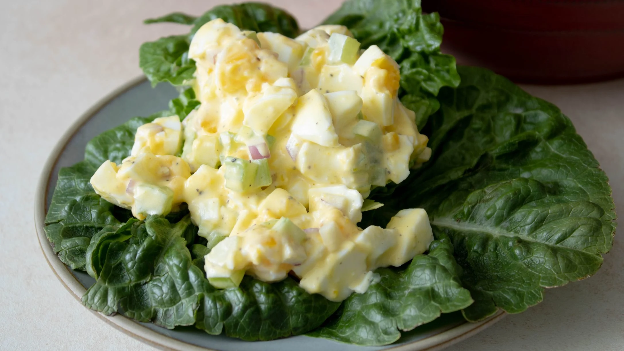 Creamy egg salad with celery and red onion served on a bed of fresh green lettuce leaves on a gray plate.