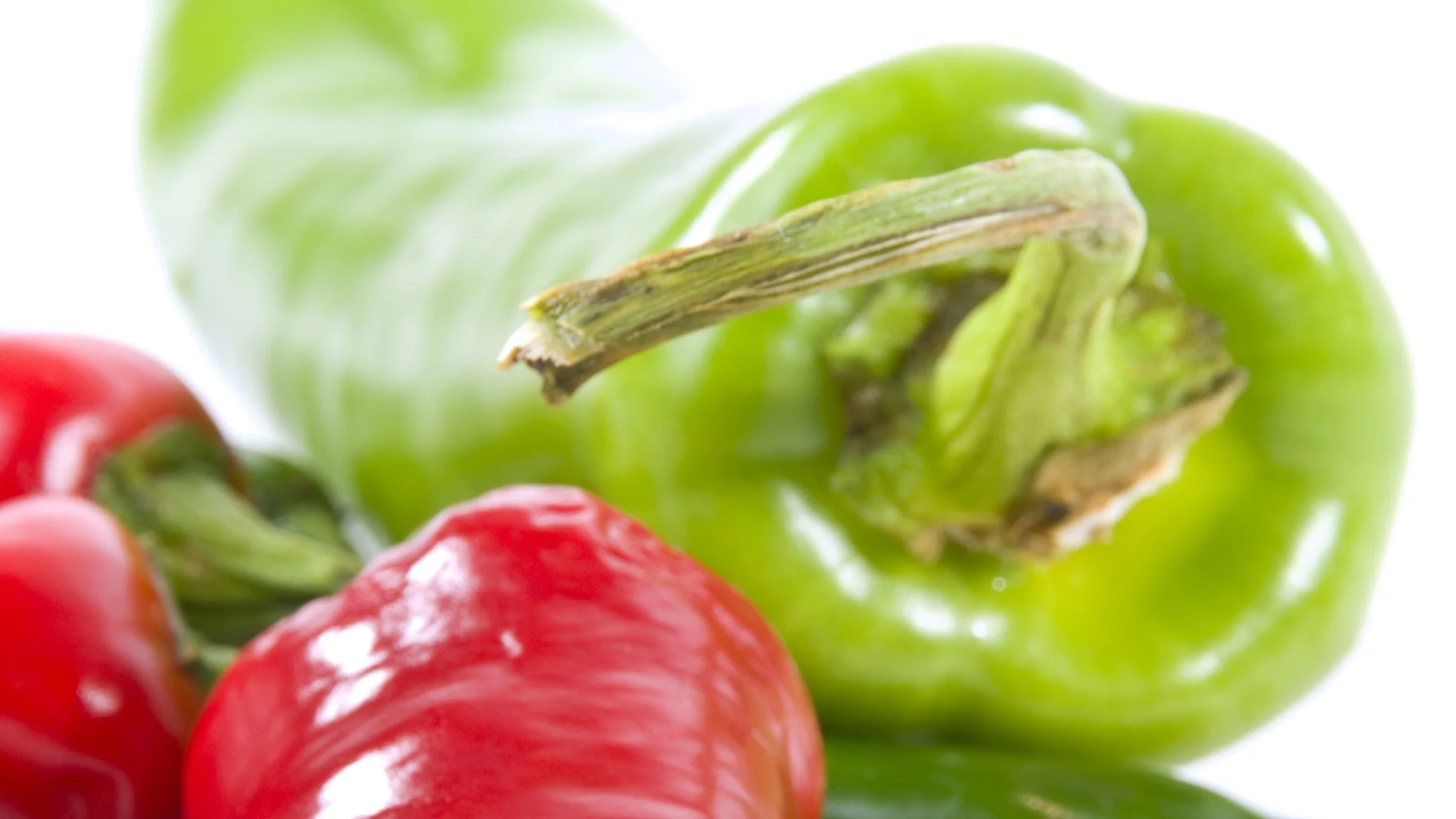 Close-up of fresh red and green bell peppers on a white background, with a shallow depth of field.