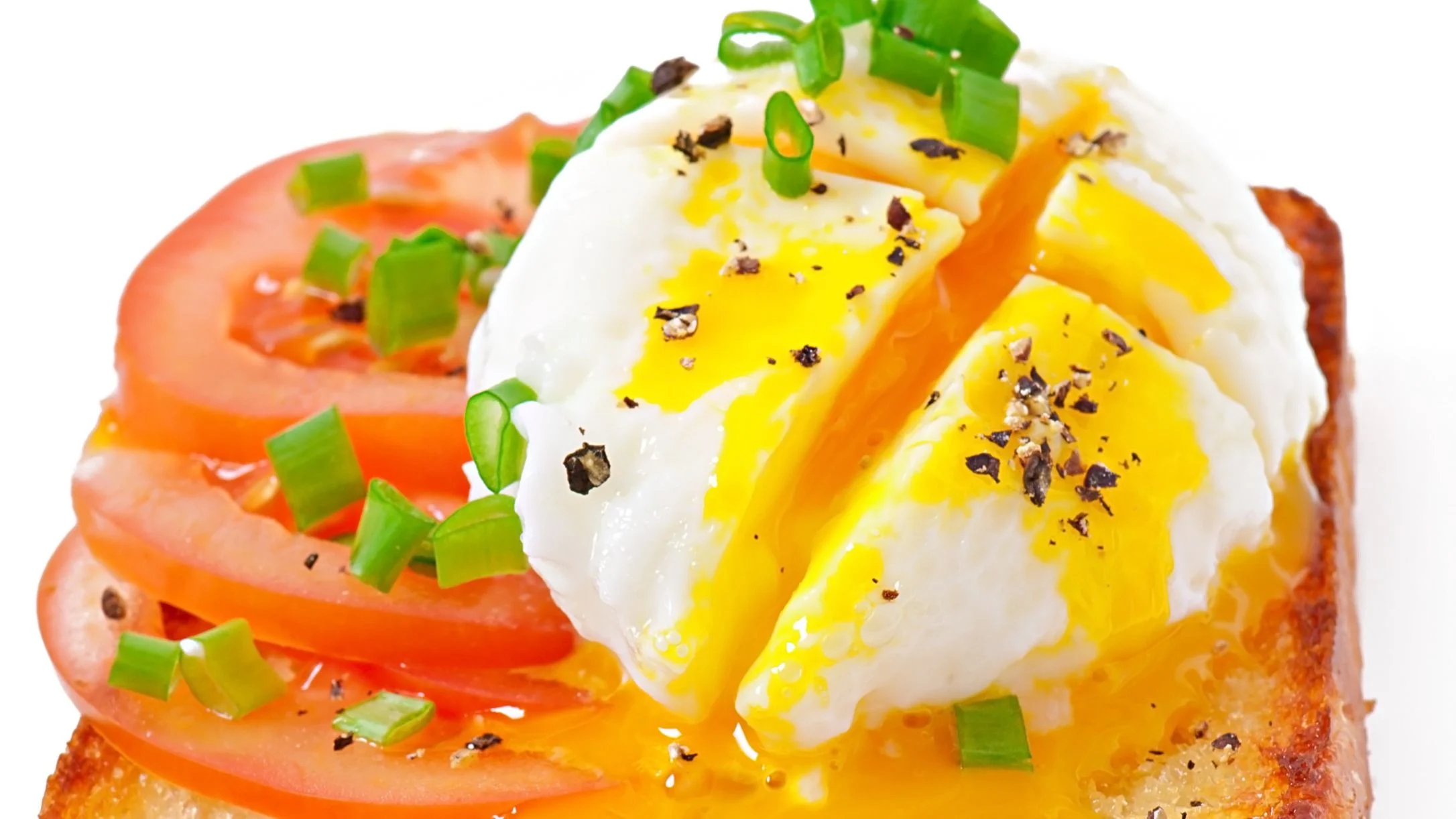 A poached egg with runny yolk topped with tomato slices, chopped green onions, and black pepper.